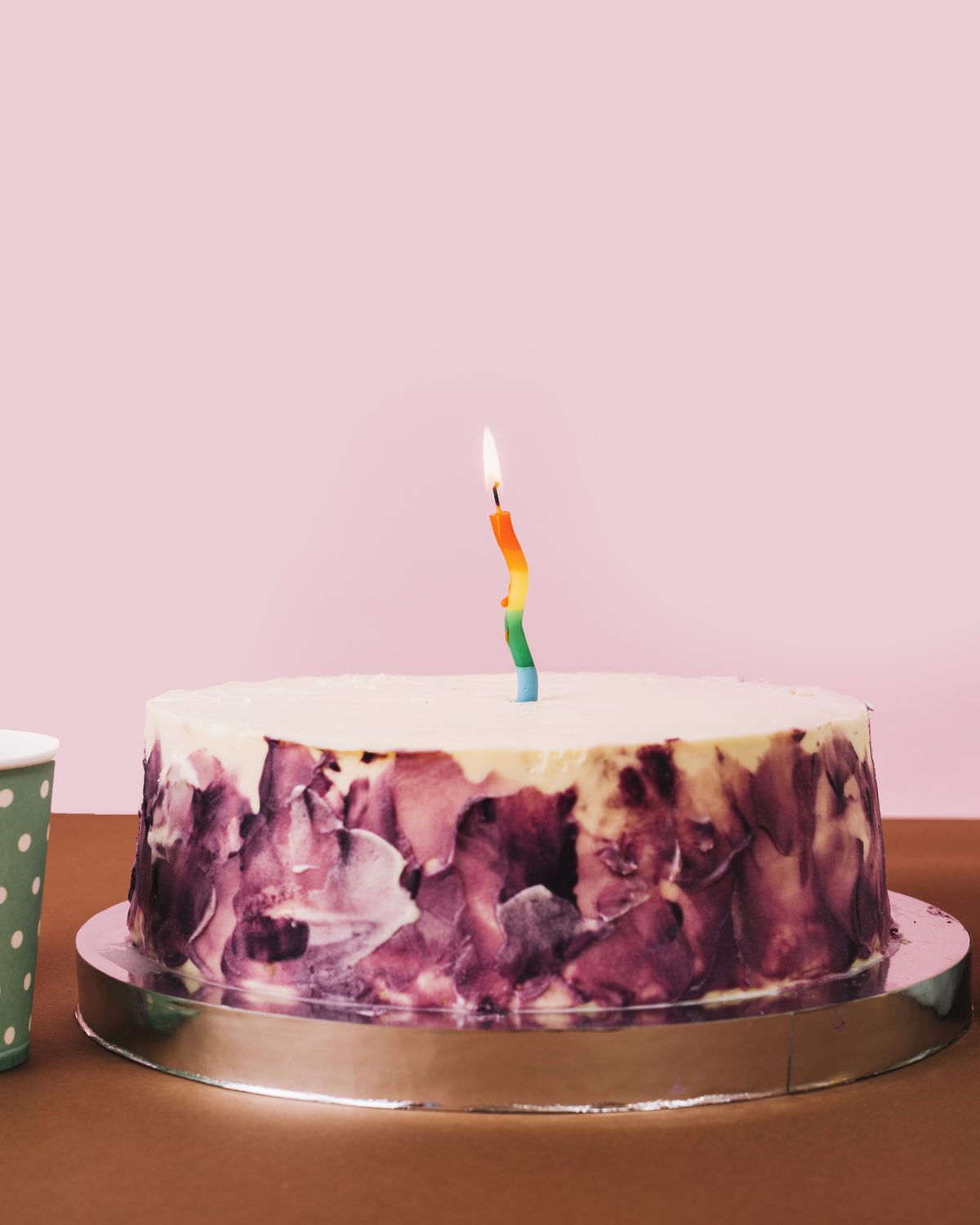 Birthday cake with candle, pink backdrop and gift box